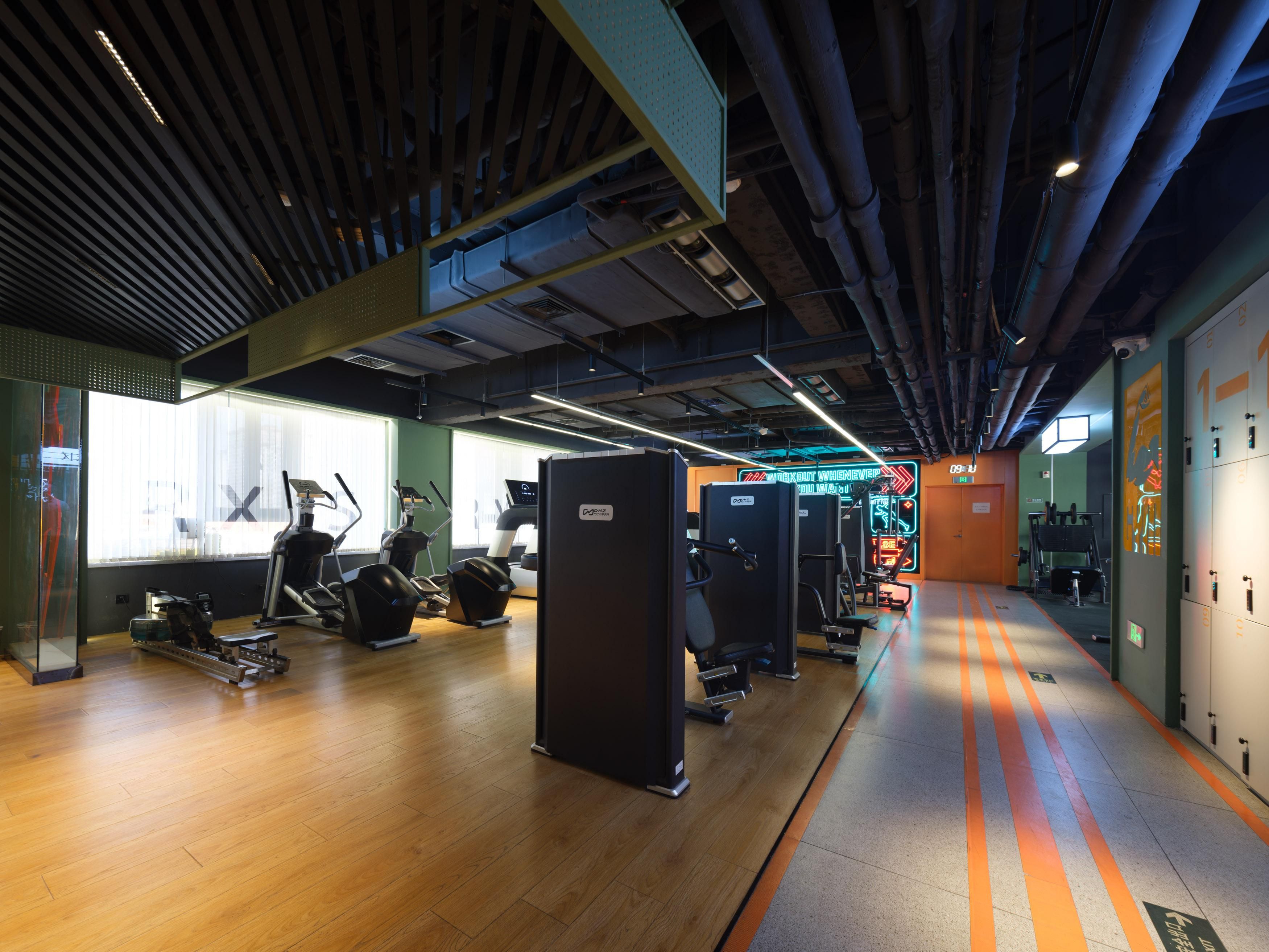 Een fitnessruimte met trainingsapparatuur, een houten vloer en een gang met kluisjes.