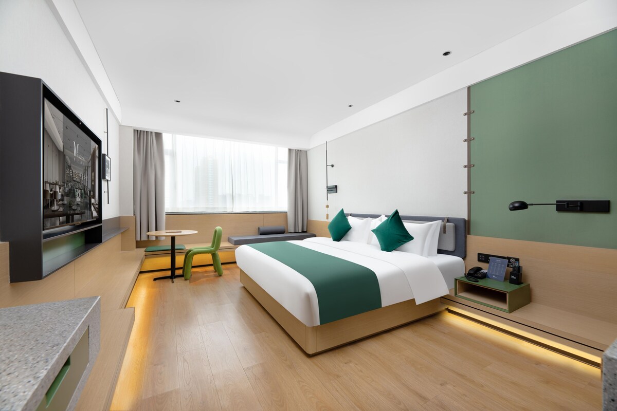 Una habitació d'hotel moderna amb un llit gran, una taula petita, una cadira, un televisor i una finestra amb cortines.