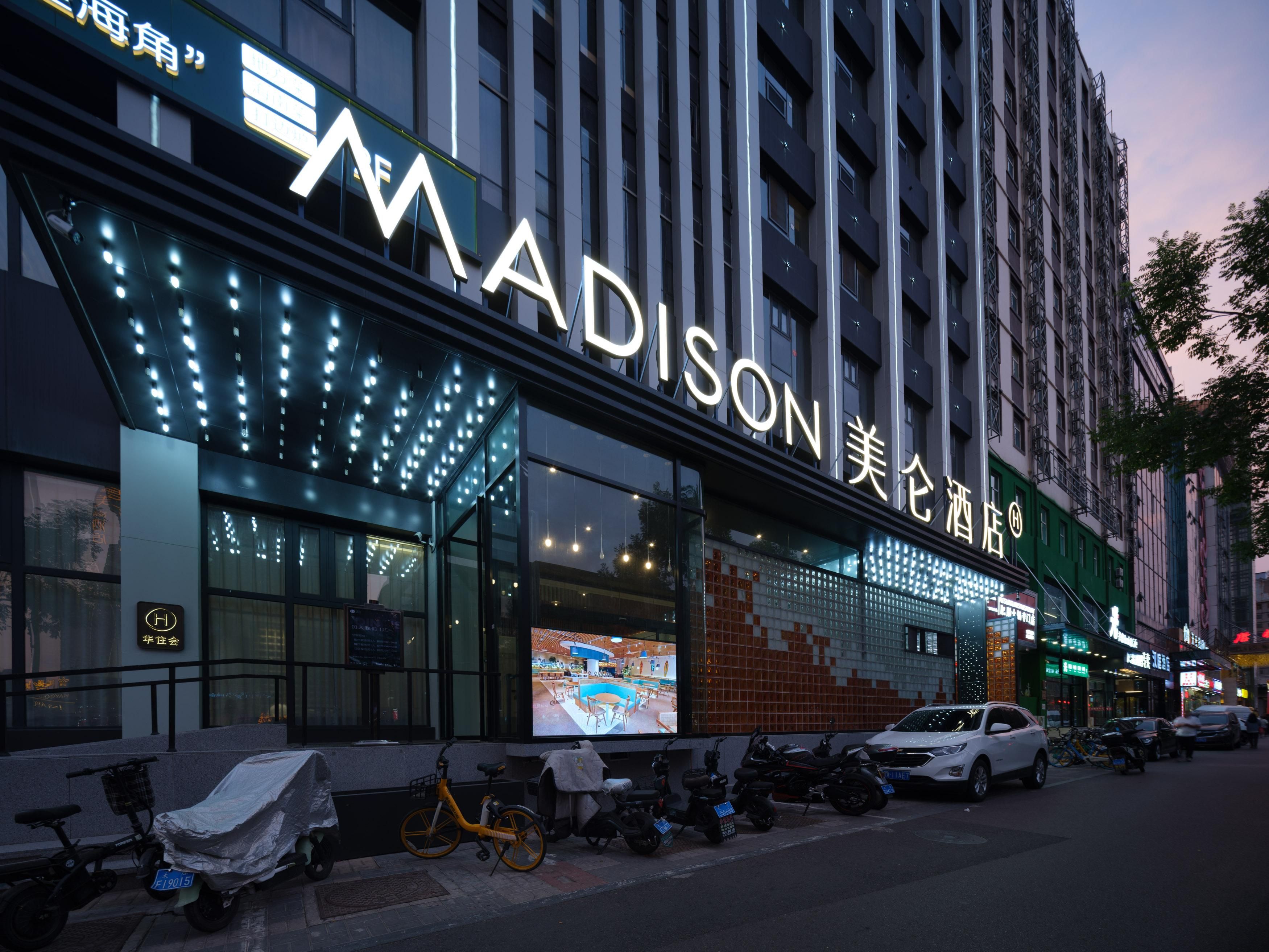 Un hotel con un gran letrero iluminado, zona de estar al aire libre y vehículos estacionados.