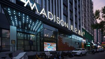 A hotel with a large illuminated sign, outdoor seating area, and parked vehicles.