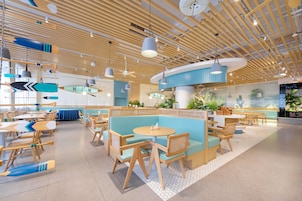 A modern interior with wooden ceiling beams, round tables, and blue seating areas.