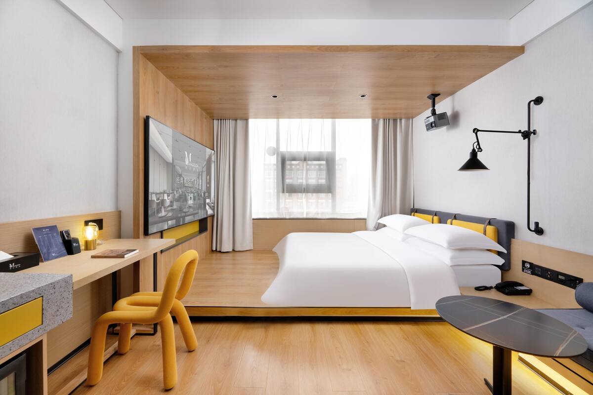 Una habitación de hotel moderna con cama, escritorio, silla y un ventanal grande.