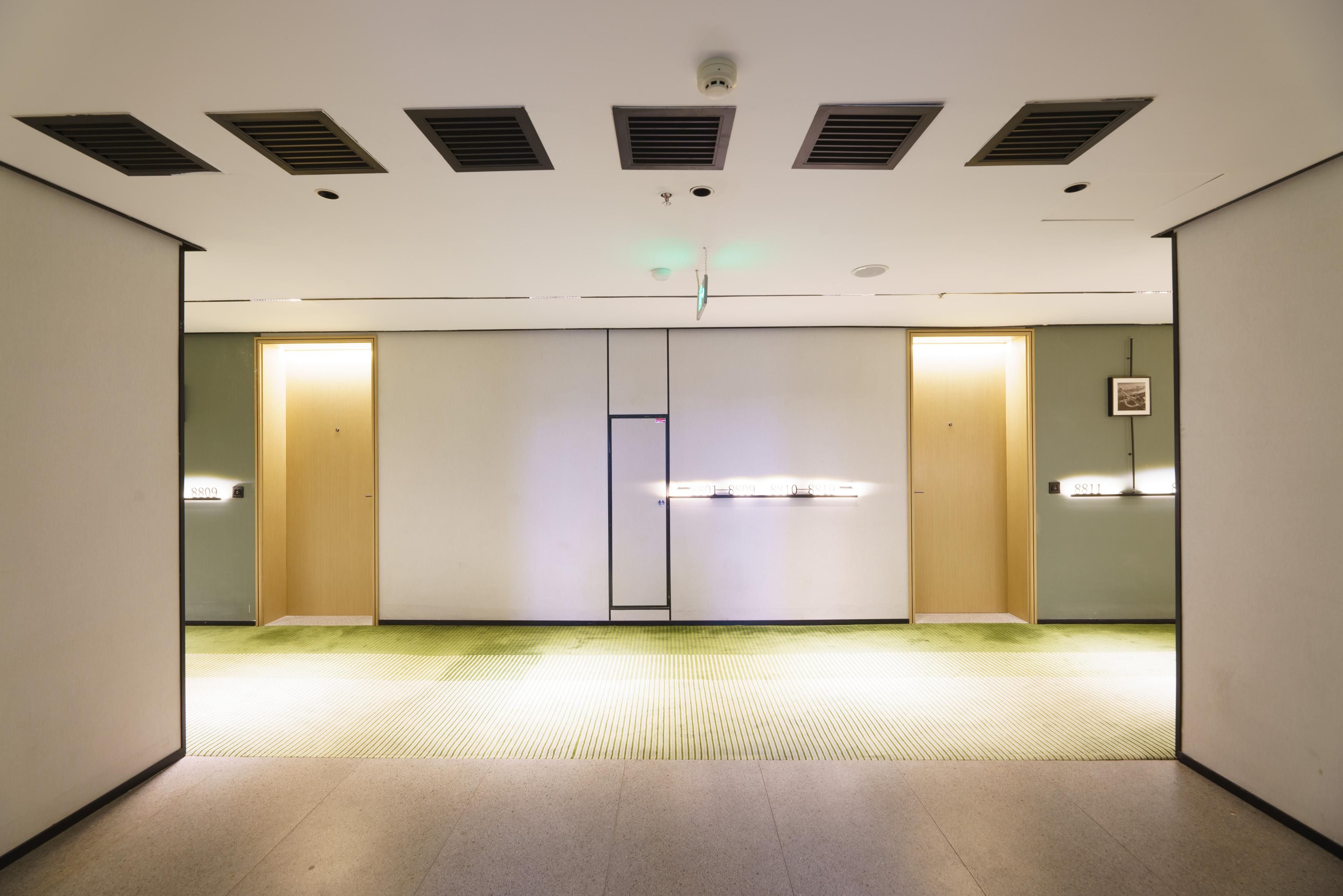 Un couloir avec un mur recouvert de miroirs, une porte éclairée et un plafond doté de bouches d’aération.