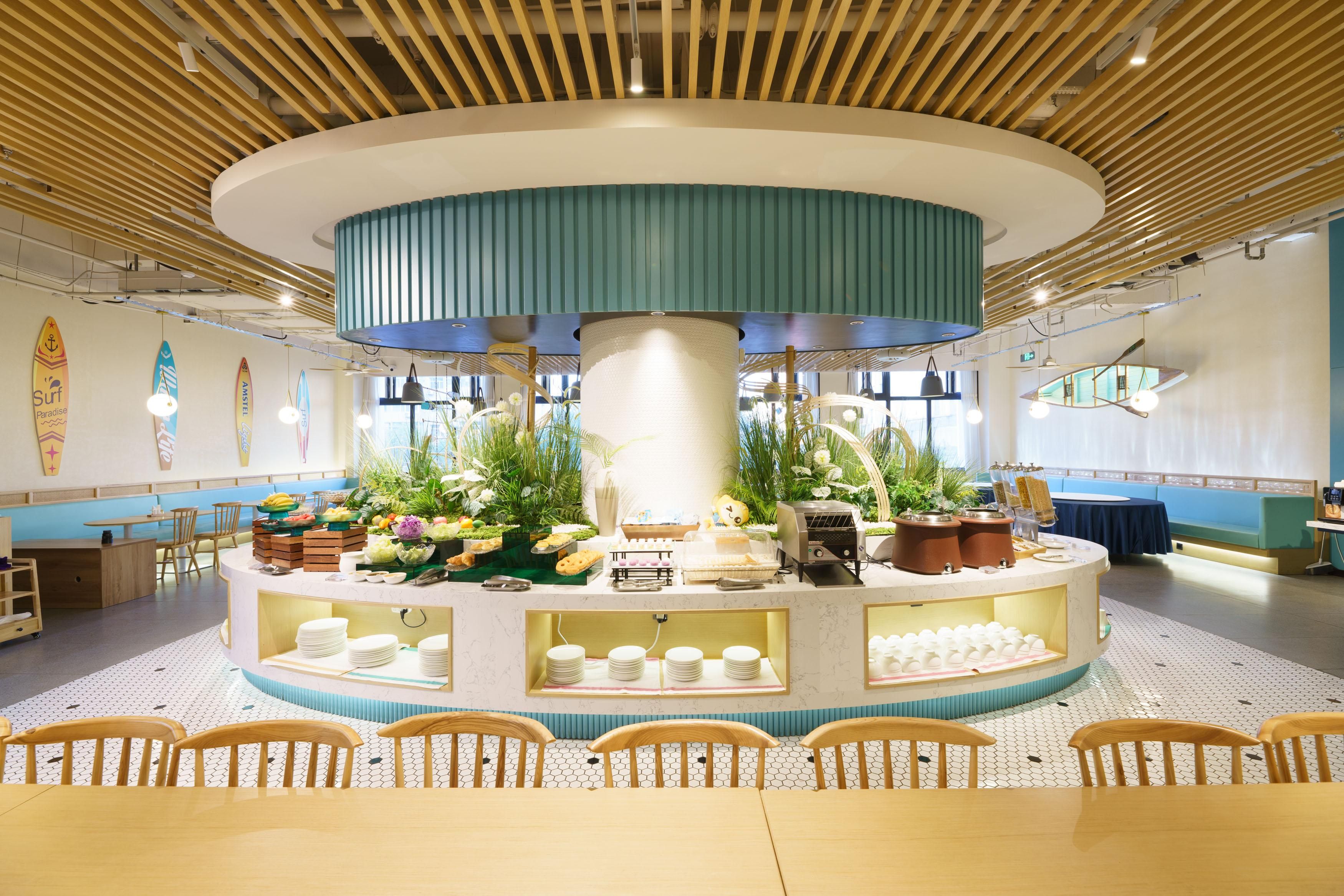 Un espace d’accueil circulaire avec un pilier central, entouré de tables et de chaises, et un buffet.