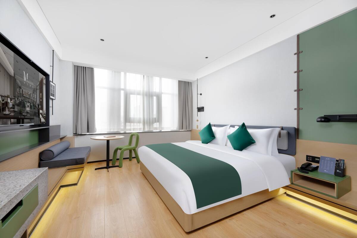 Una habitación de hotel moderna con cama, mesita de noche, silla y una pequeña mesa con lámpara.