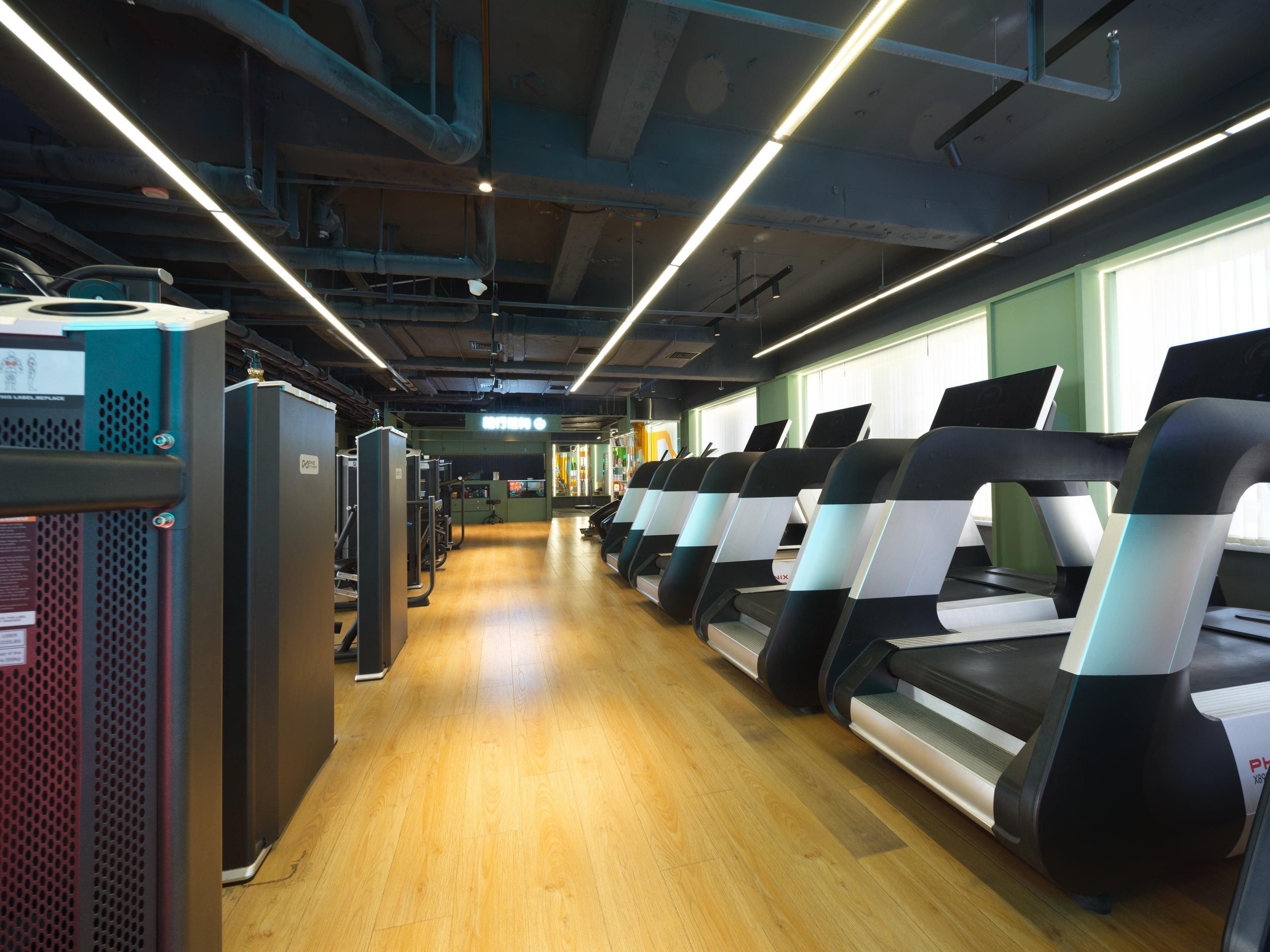 A gym with treadmills, exercise equipment, and a wooden floor.