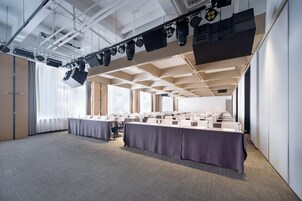 Un salón de conferencias con una larga mesa, iluminación en el techo y suelo alfombrado.