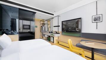 A modern hotel room with a large bed, a seating area with a round table, a TV, and a wardrobe.