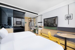 A modern hotel room with a large bed, a seating area with a round table, a TV, and a wardrobe.