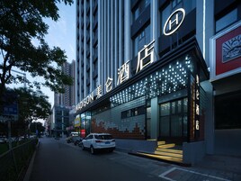 A modern hotel with a prominent sign, a staircase leading to the entrance, and a parking area.