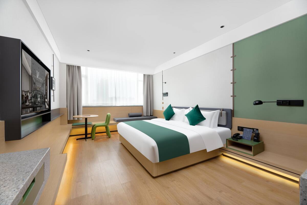Una habitación de hotel moderna con una cama grande, una mesita, una silla, un televisor y una ventana con cortinas.