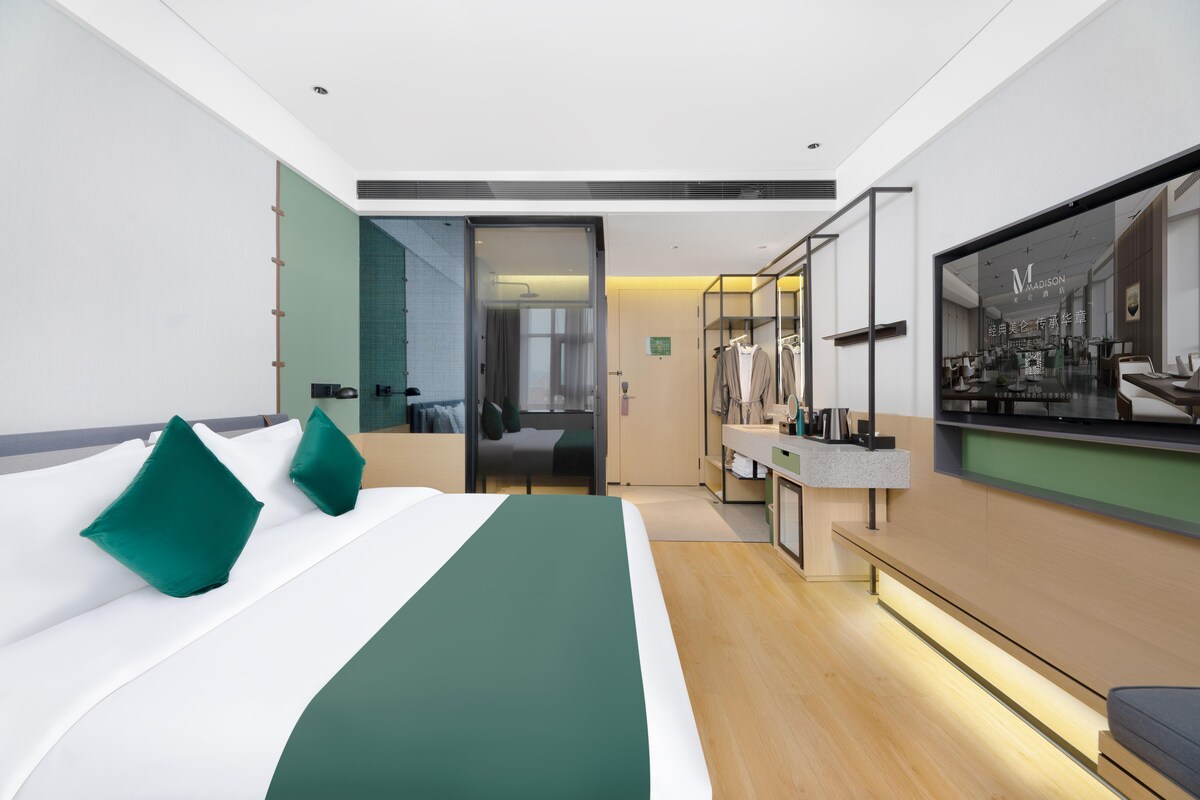 Una habitació d'hotel moderna amb un llit gran, una tocador amb mirall i vista a la ciutat.