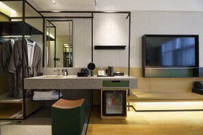 Ein modernes Badezimmer mit Waschtisch, Spiegel, Handtuchhalter, kleinem Kühlschrank und einem an der Wand montierten Fernseher.