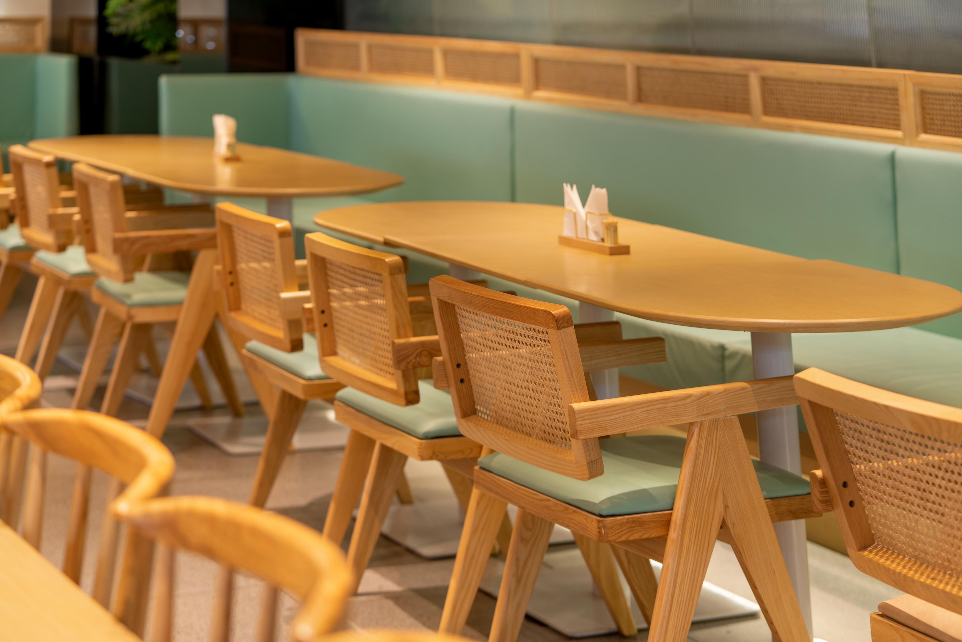 A restaurant with wooden tables and chairs, green cushioned booths, and a tiled backsplash.