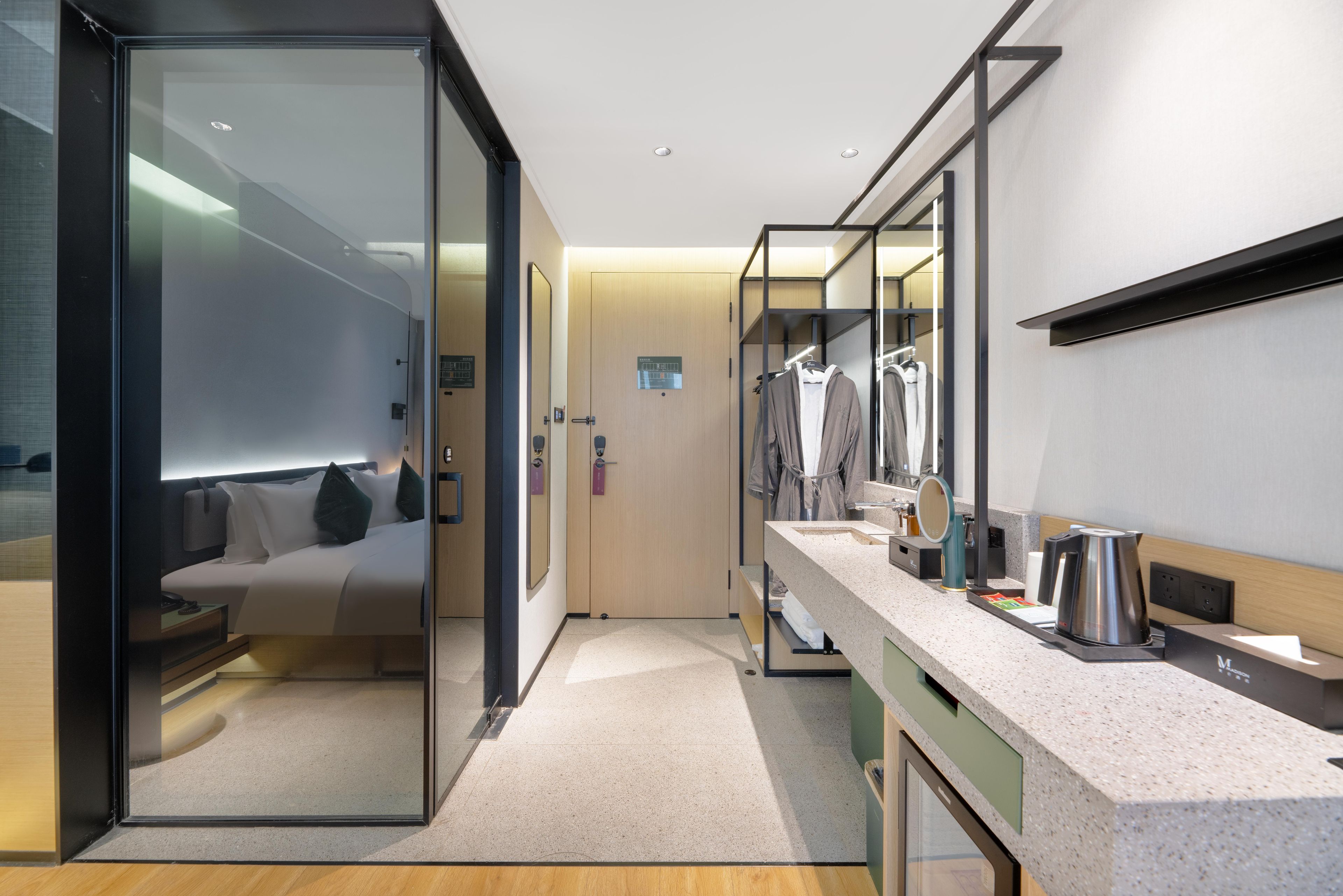Una habitación de hotel moderna con un separador de vidrio, una cama, un tocador con espejo, un lavabo y una cafetera.