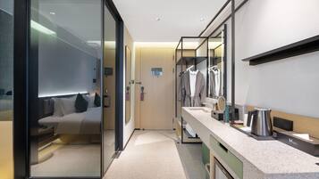 Una habitación de hotel moderna con un separador de vidrio, una cama, un tocador con espejo, un lavabo y una cafetera.