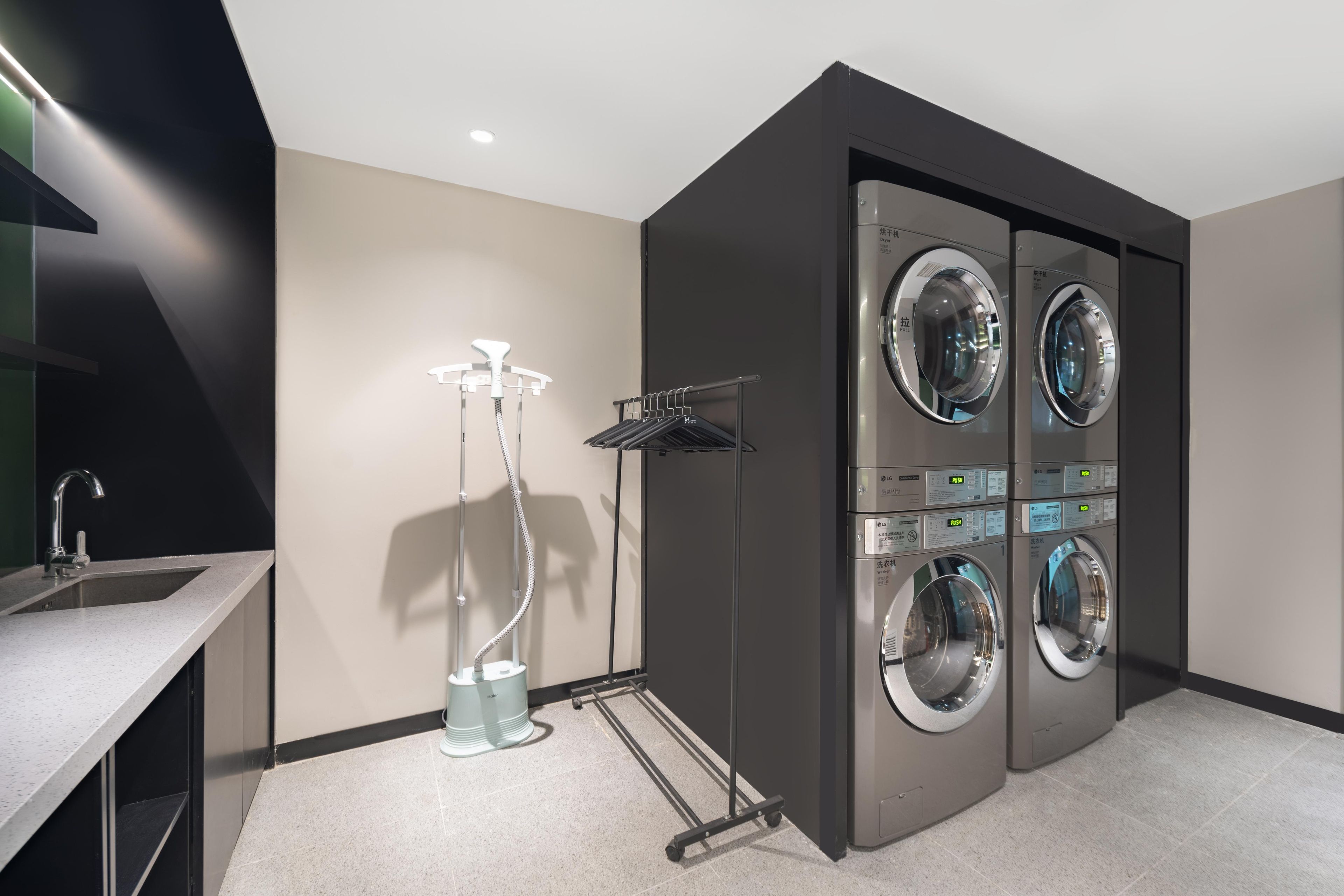 A modern laundry room with four wall-mounted washing machines, a drying rack, and a vacuum cleaner.