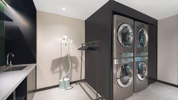 A modern laundry room with four wall-mounted washing machines, a drying rack, and a vacuum cleaner.