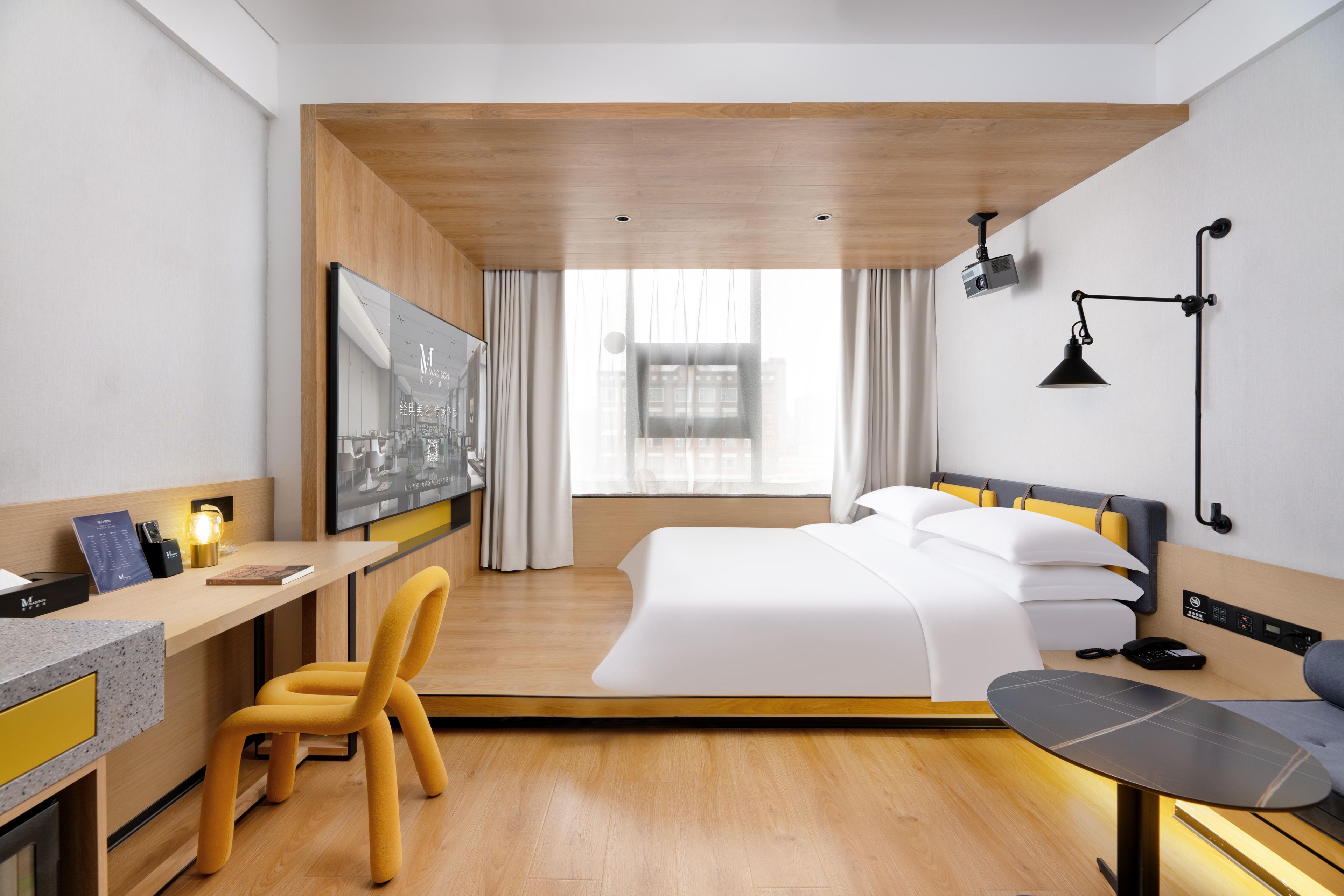 Een moderne hotelkamer met een bed, bureau, stoel en een groot raam.
