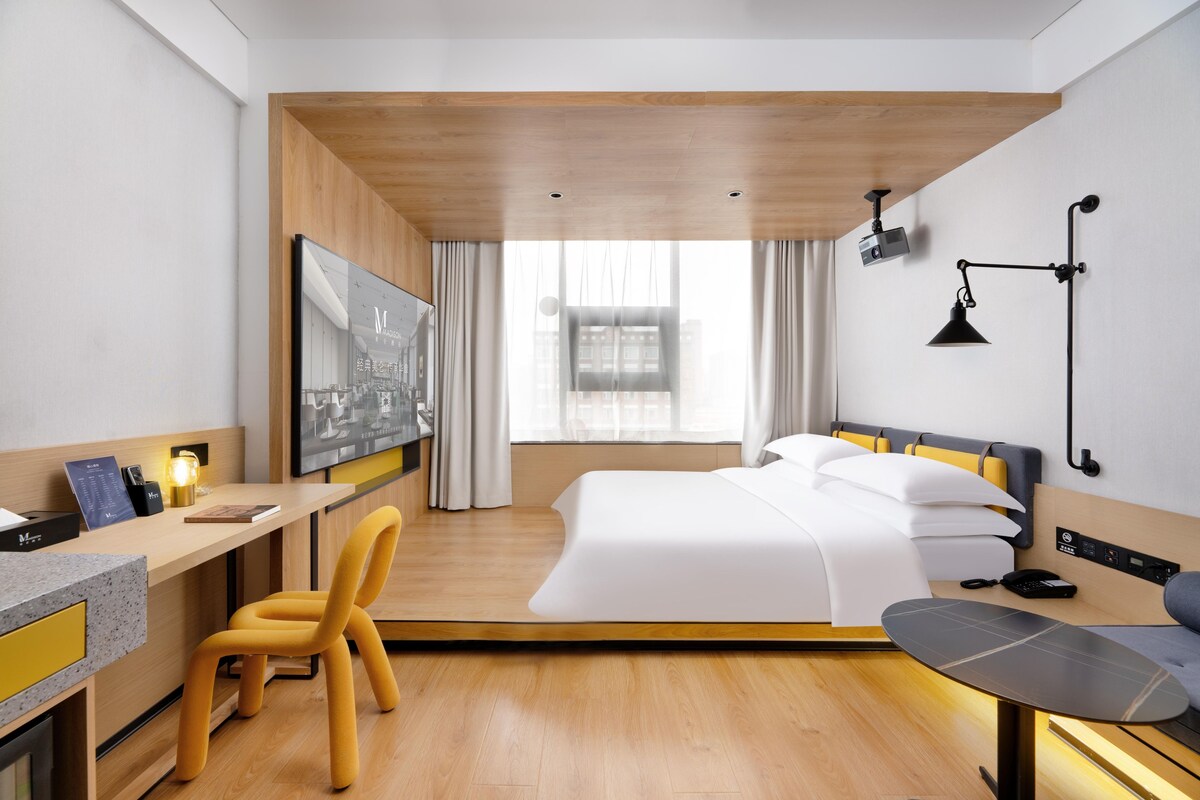 Una habitació d'hotel moderna amb un llit, escriptori, cadira i una finestra gran.
