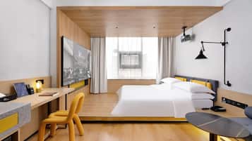 A modern hotel room with a bed, desk, chair, and a large window.