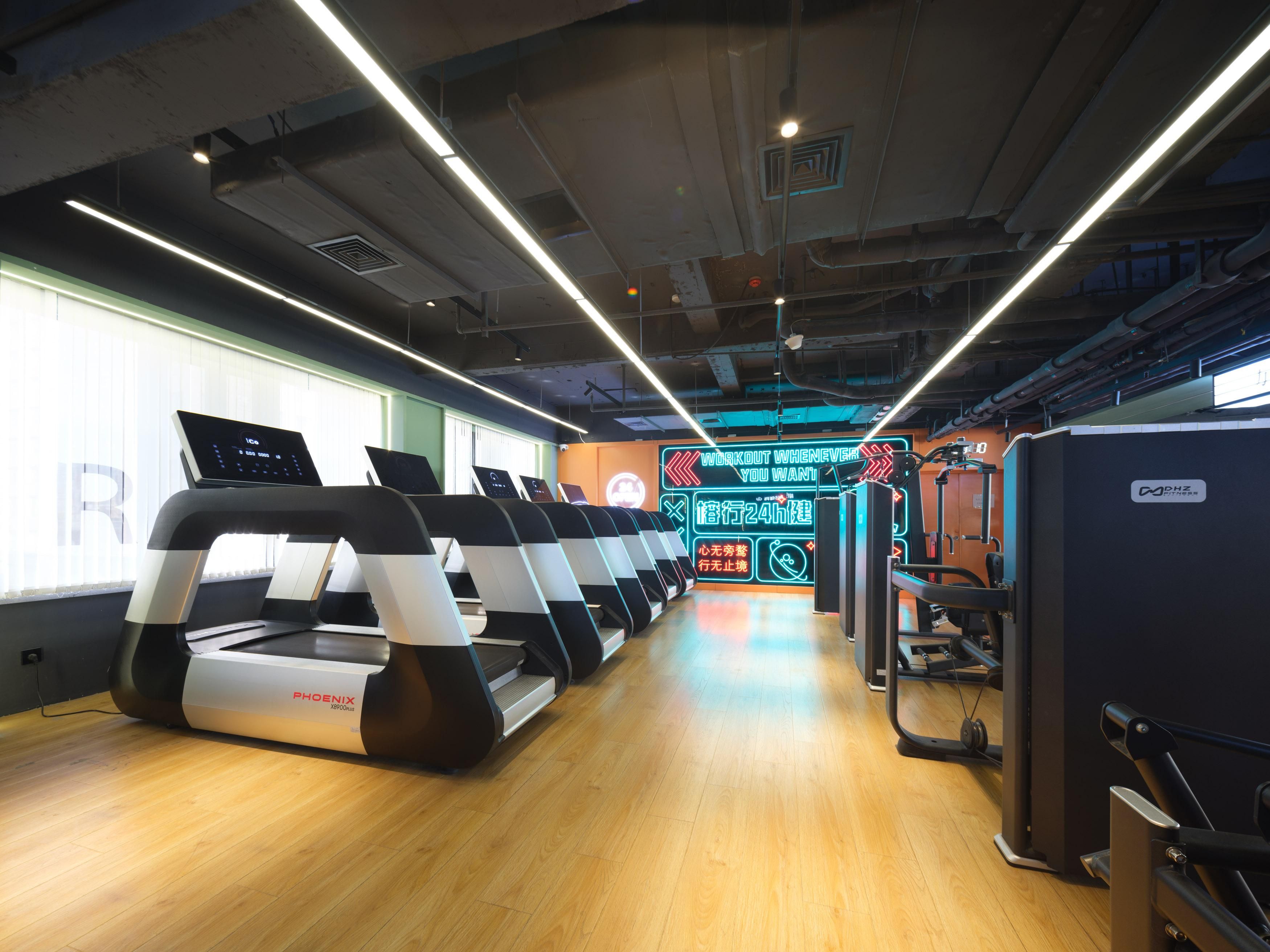Un gimnasio con cintas de correr, equipo de ejercicio y una pantalla digital.