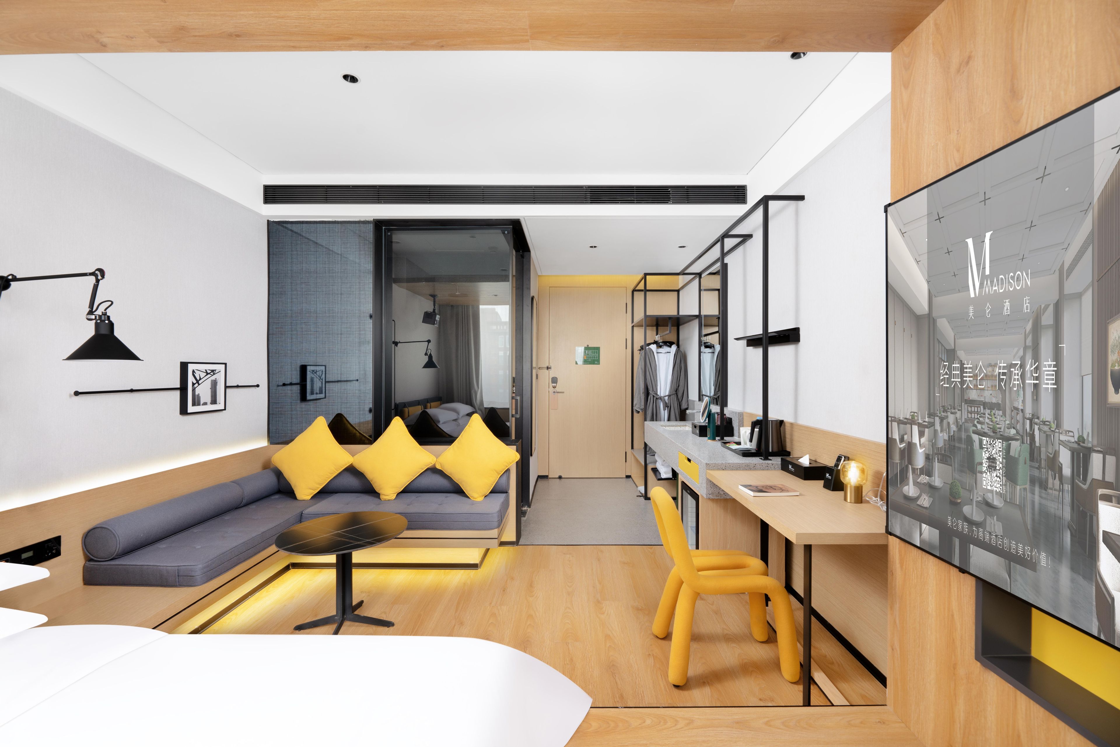 Una habitación de hotel moderna con sofá, mesa de comedor, silla amarilla, televisión y armario.