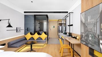 A modern hotel room with a sofa, a dining table, a yellow chair, a TV, and a wardrobe.