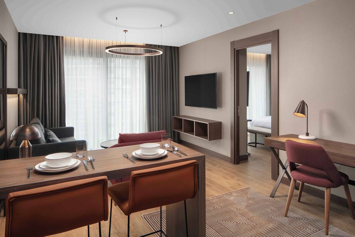 Ein modernes Hotelzimmer mit Essbereich, einem an der Wand befestigten Fernseher und Blick auf die Stadt.