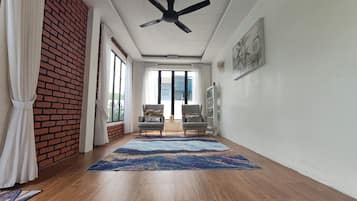 Een kamer met een plafondventilator, twee fauteuils, een groot vloerkleed en uitzicht door een glazen deur.