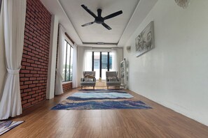A room with a ceiling fan, two armchairs, a large rug, and a view through a glass door. - Aeden Villa Roomstay & Homestay By Zuzu (Kuala Kangsar)