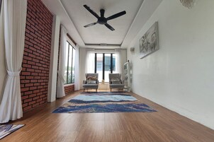 Quarto com ventoinha no teto, duas poltronas, um tapete grande e vista através de uma porta de vidro.