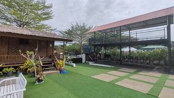 A courtyard with artificial grass, a wooden structure, and a metal building with a red roof.