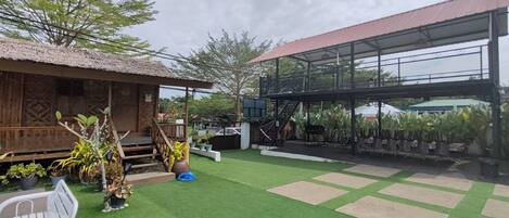 A courtyard with artificial grass, a wooden structure, and a metal building with a red roof.