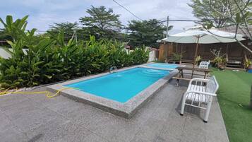 Une piscine rectangulaire dont le bord est recouvert de carrelage, entourée d’un espace patio avec une chaise blanche et une table.