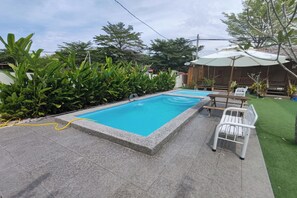 Ein rechteckiger Pool mit gefliestem Rand, umgeben von einer Terrasse mit einem weißen Stuhl und einem Tisch.