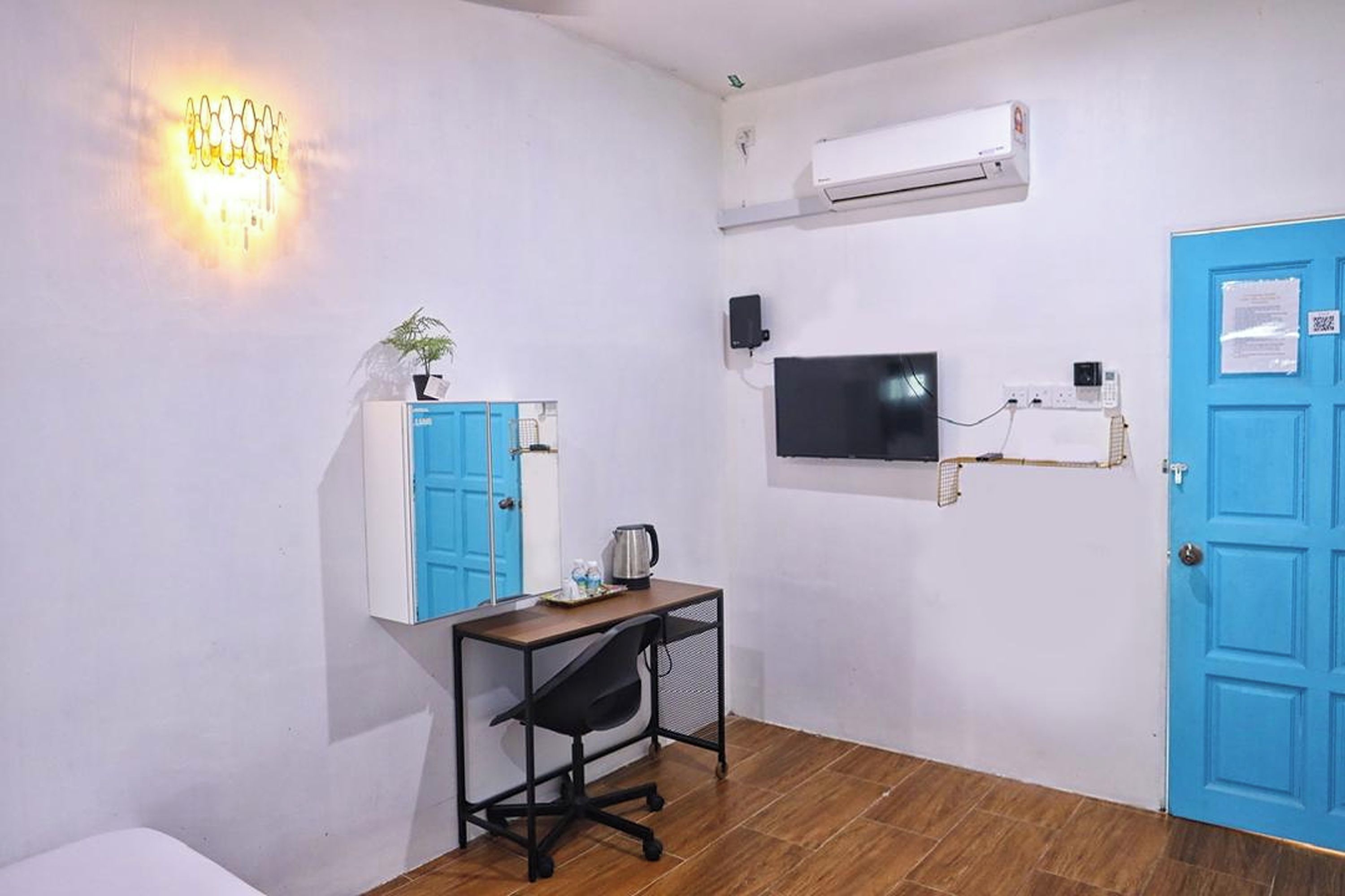 A room with a desk, chair, blue wardrobe, wall-mounted TV, air conditioning unit, and a blue door.