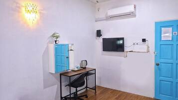 A room with a desk, chair, blue wardrobe, wall-mounted TV, air conditioning unit, and a blue door.