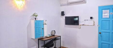 A room with a desk, chair, blue wardrobe, wall-mounted TV, air conditioning unit, and a blue door.