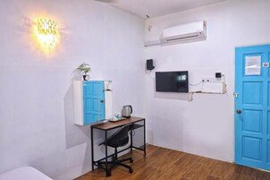 Una habitación con escritorio, silla, armario azul, televisor montado en la pared, unidad de aire acondicionado y una puerta azul.
