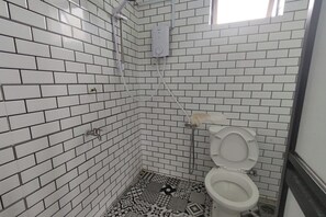 A bathroom with white tiled walls, a patterned floor, a toilet, and a shower head.