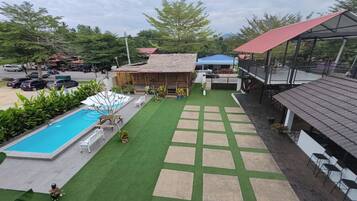A pool area with a wooden structure, a covered seating area, and a paved walkway.