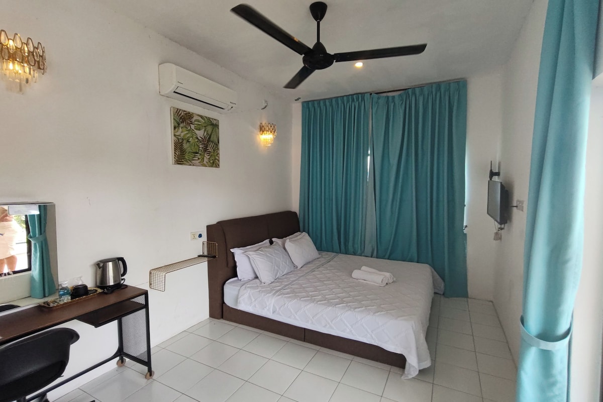 A hotel room with a bed, a desk with a chair, a ceiling fan, and a window with curtains.