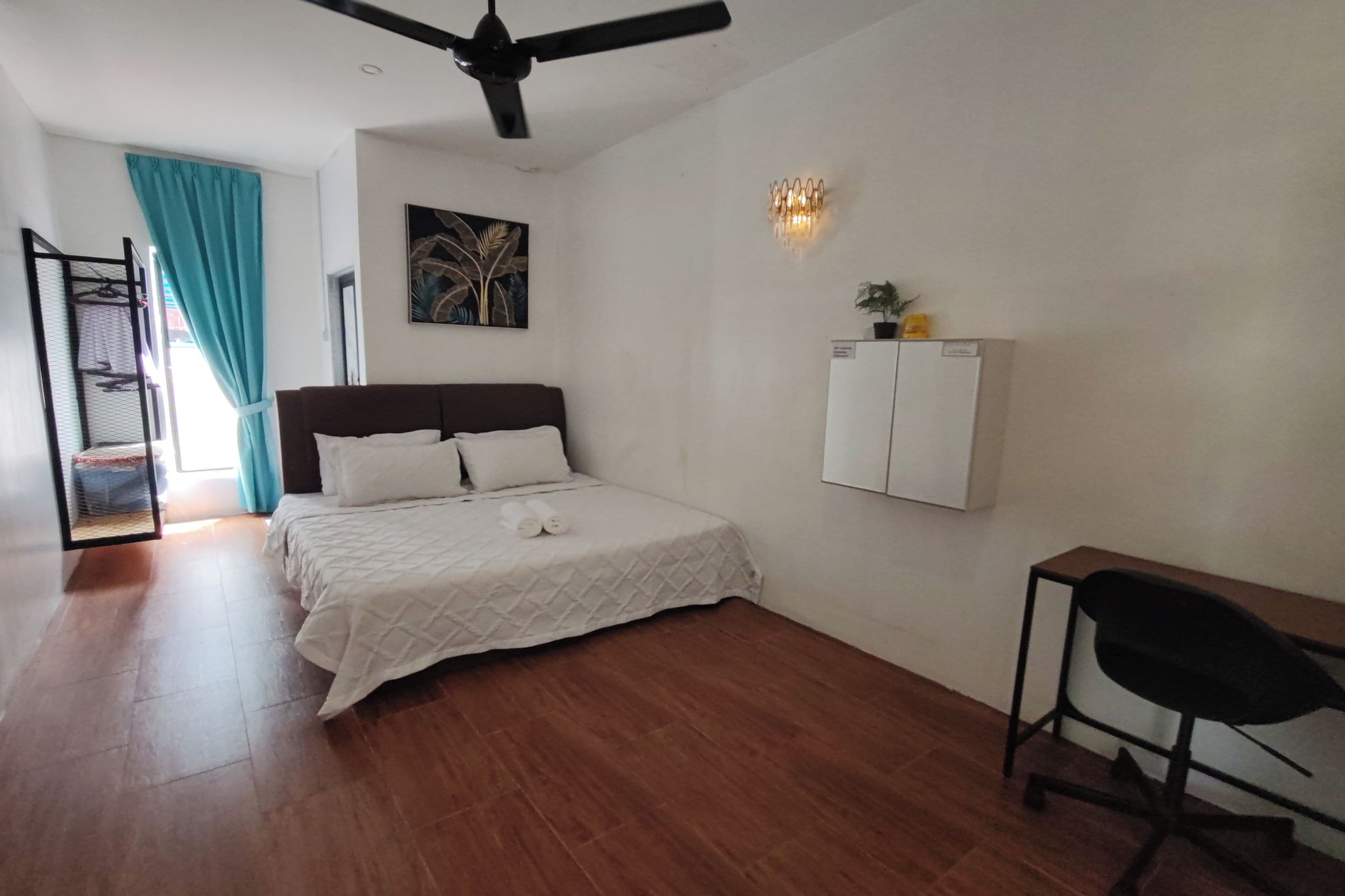 Ein Schlafzimmer mit einem Bett, einem Schreibtisch, einem Sessel, einem Deckenventilator, einem an der Wand befestigten Schrank und einem Gemälde.