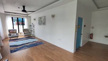 A spacious living area with a large window, a ceiling fan, and a blue door.