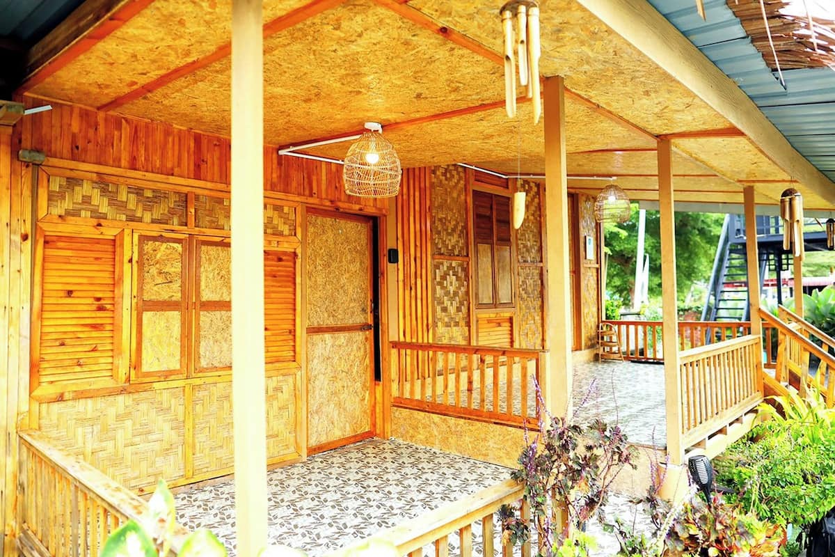 Une cabane en bois dotée d’un porche couvert, d’un luminaire en fibres tressées et offrant une vue sur la verdure environnante.