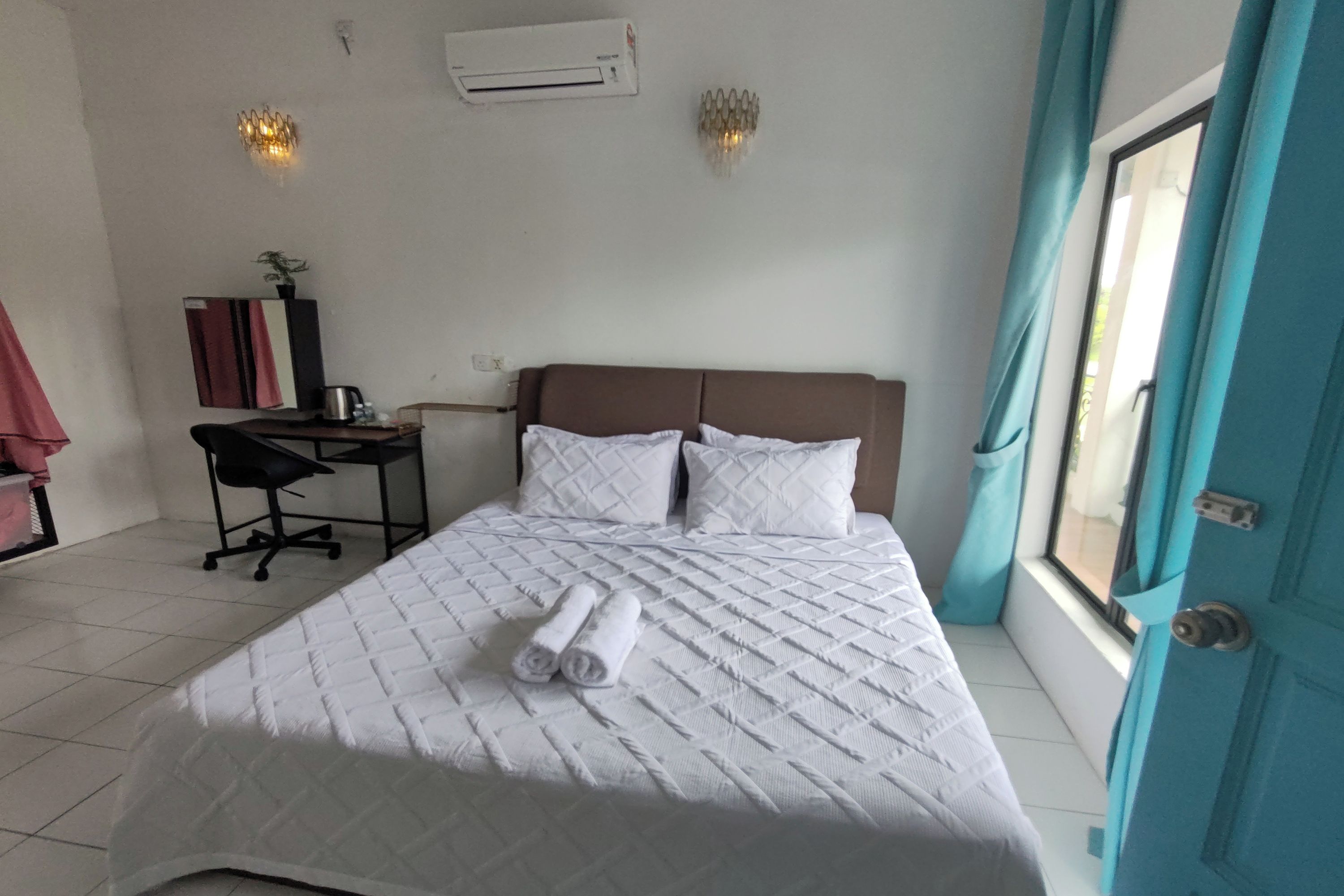 A hotel room with a bed, a desk, a chair, an air conditioner, and a window with curtains.