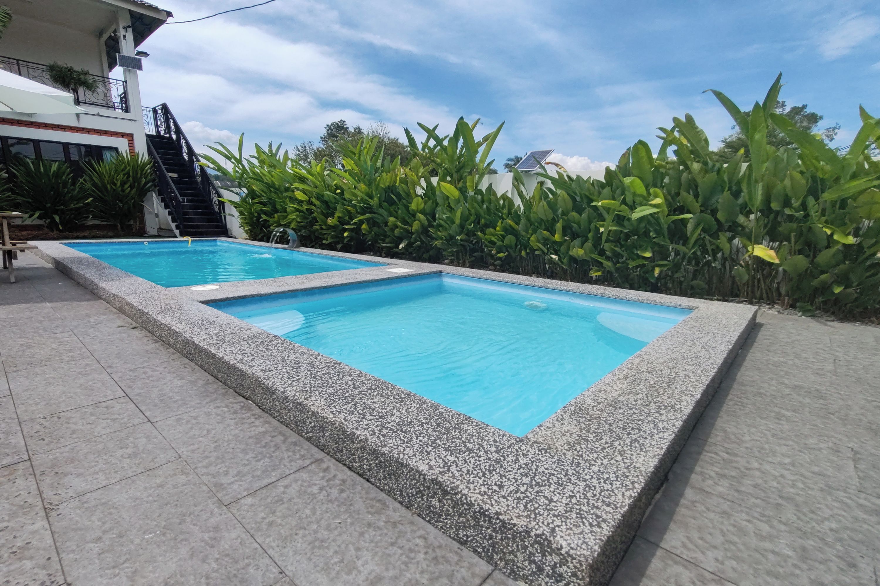 A rectangular pool with a stone border, surrounded by a tiled patio.