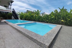 Piscina retangular com borda de pedra, rodeada por um terraço ladrilhado.