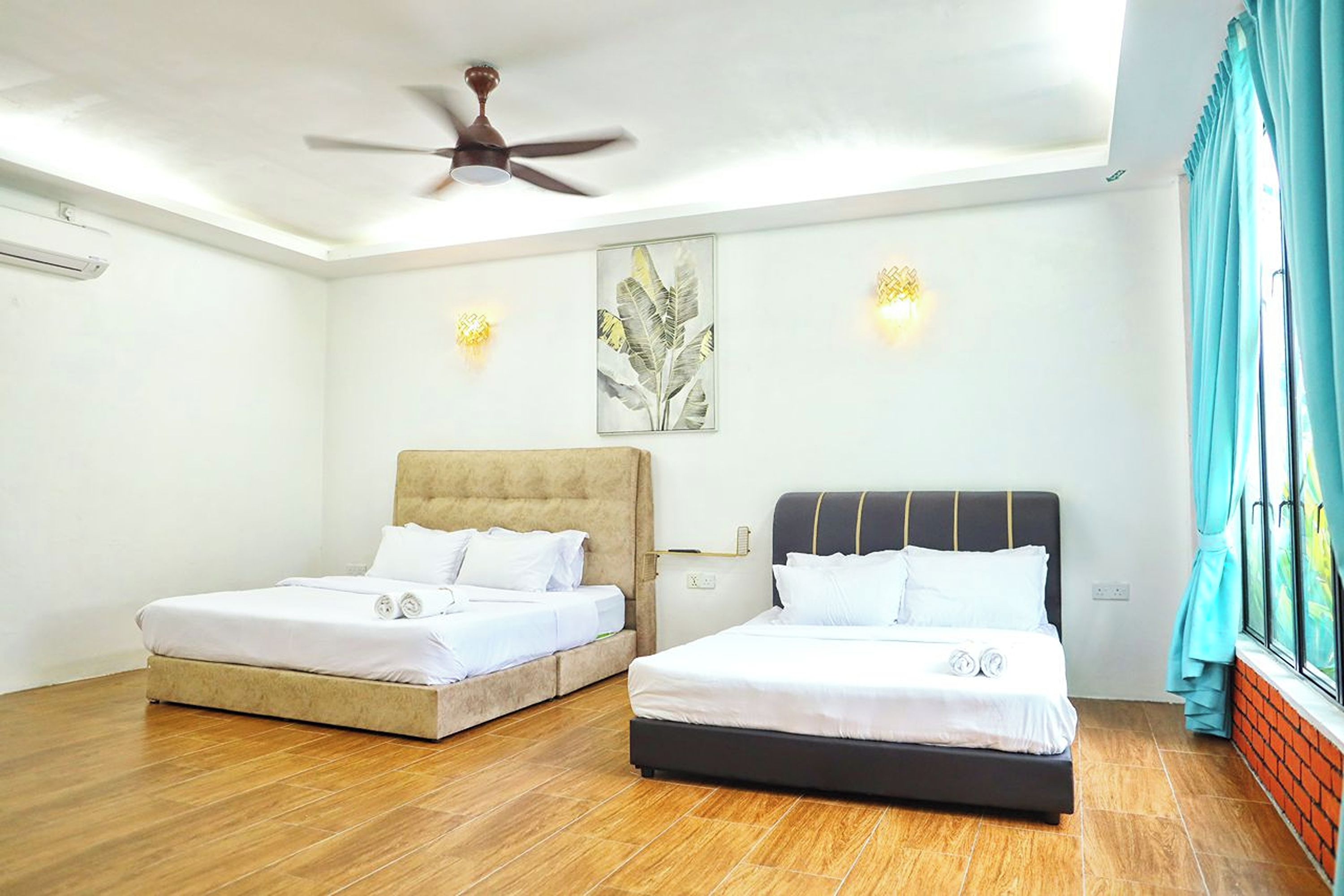 A hotel room with two beds, a ceiling fan, wall-mounted lights, and a window with curtains.